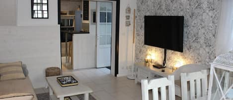 Een woonkamer met een bank, een salontafel, een televisie en een kleine tafel met een lamp. Er is een deur die leidt naar een keuken.