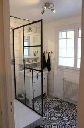A bathroom with a shower enclosure, white tiles, a radiator, and a window.