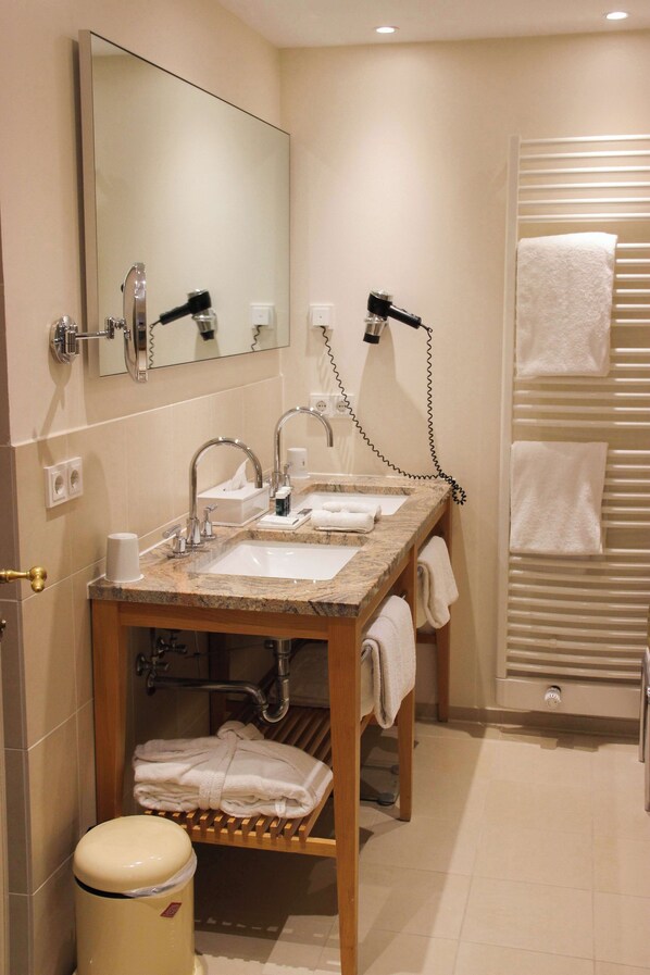 Une salle de bain avec deux lavabos, un miroir, un porte-serviettes et une poubelle.