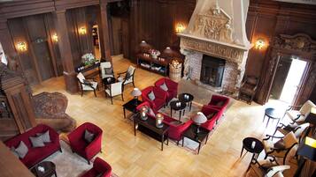 A spacious lobby with a high ceiling, wooden paneling, and a fireplace. There are multiple seating areas with red and white furniture, and a small table with candles.