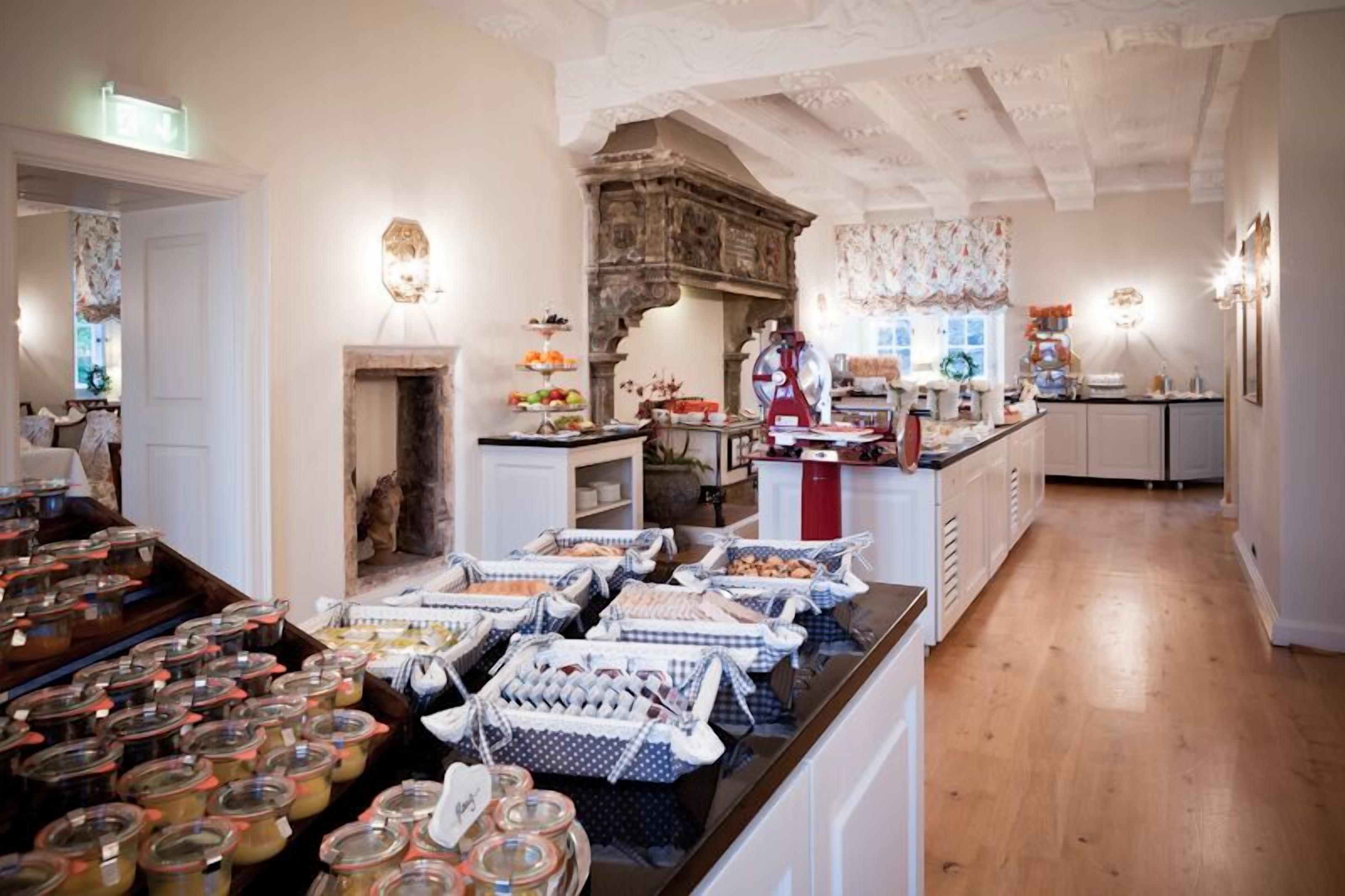 A spacious kitchen with a wooden floor, a central island with various food items, and a decorative fireplace.