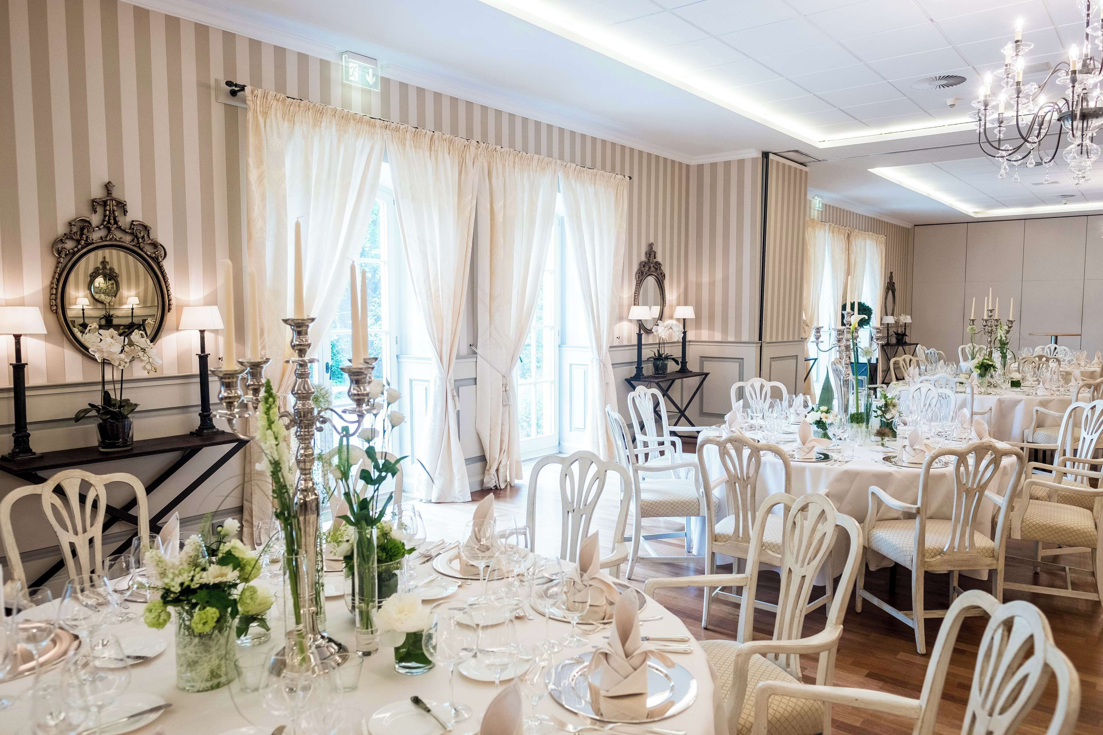 Une salle à manger élégante, avec un papier peint à rayures, des lustres et des meubles blancs.