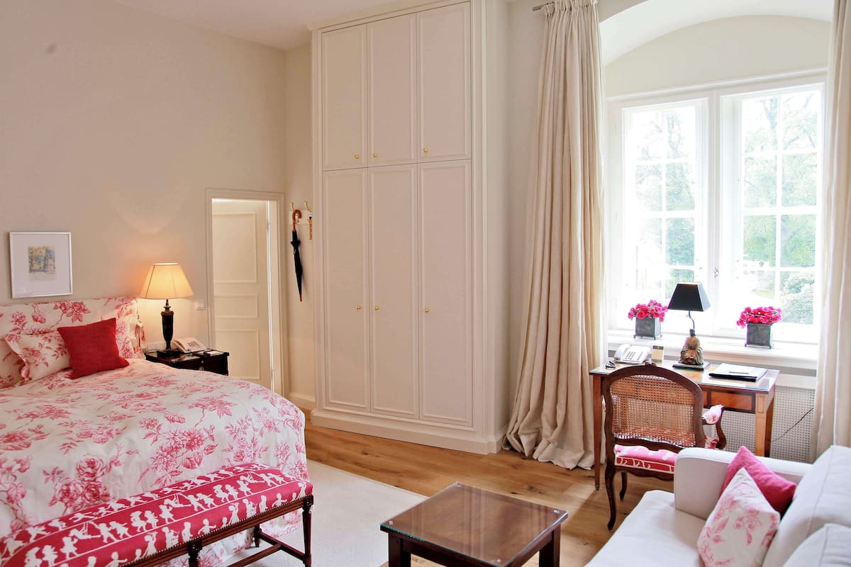 Een slaapkamer met een groot bed, een kledingkast, een bureau met stoel, en een raam met gordijnen.