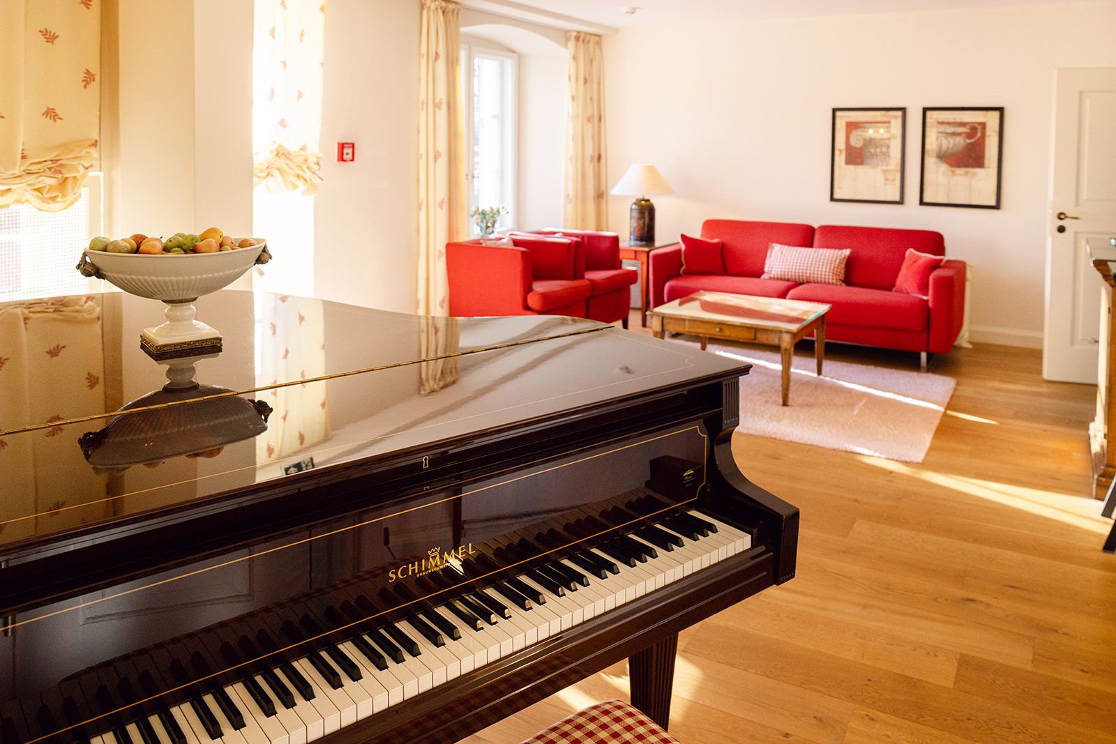 A living room with a grand piano, red sofa, and a dining area with a table and chairs.