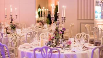 Ein Bankettsaal mit gedeckten Tischen für eine festliche Veranstaltung, mit weißen Tischdecken, Kerzenständern und floralen Tischgestecken.