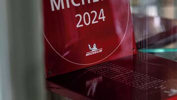 Ein rotes Schild mit dem Text "MICHELIN 2024" und einem Logo, platziert auf einem Regal mit verschiedenen Gegenständen.