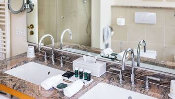 A bathroom with two sinks, a mirror, and a shower. There are toiletries on the counter.