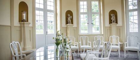 Un comedor con una mesa de vidrio, sillas blancas y estatuas sobre pedestales.