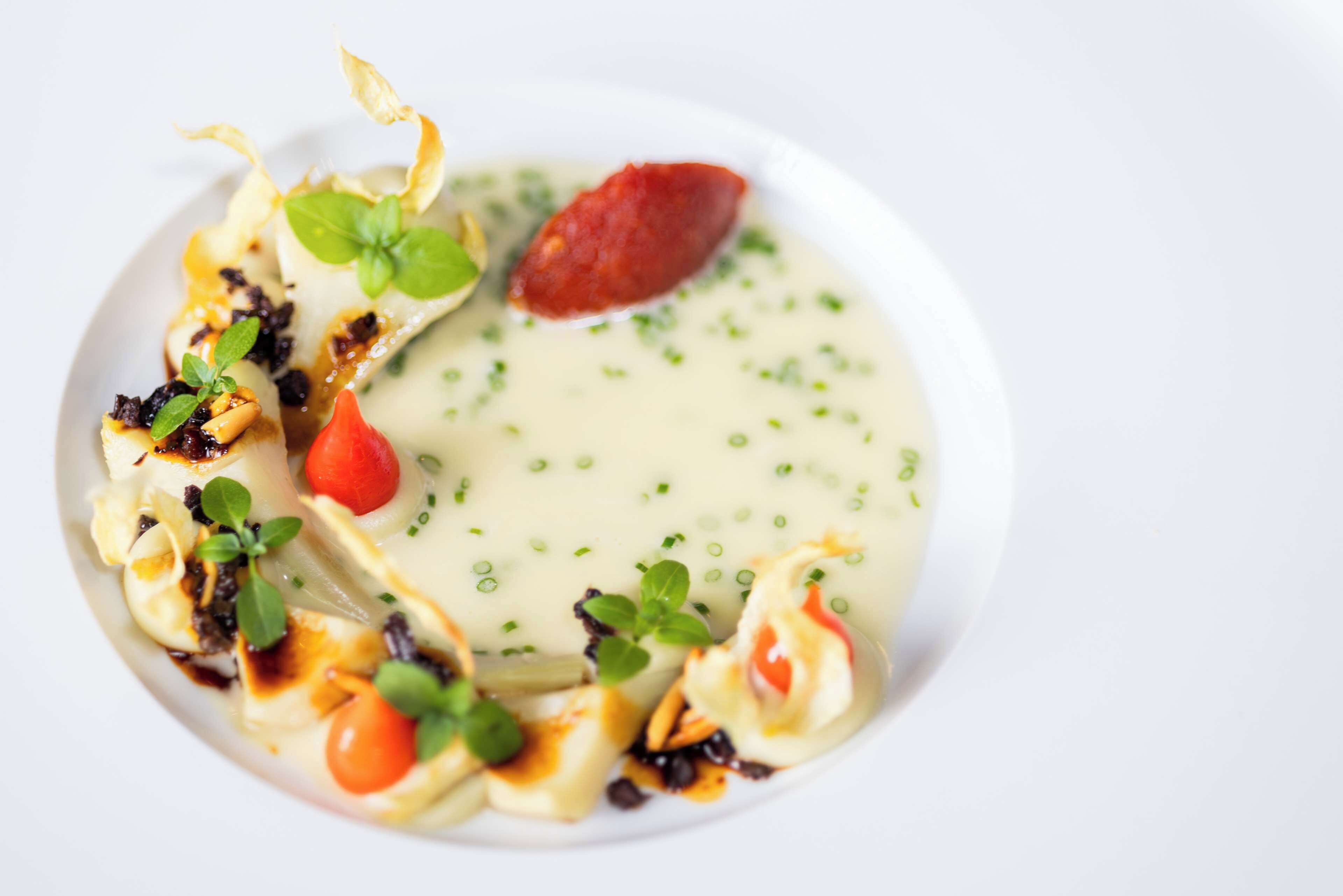 Een bord eten met ravioli, kerstomaatjes en een sausdopje.