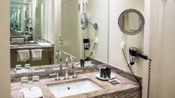 A hotel bathroom with a large mirror, a sink, and a hairdryer on the wall.