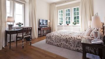 Un dormitorio con cama, escritorio, televisor y ventana con cortinas.