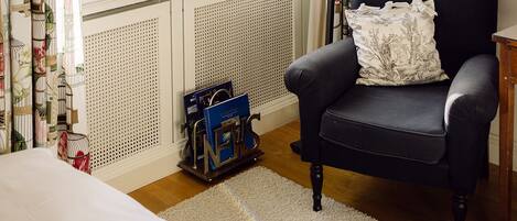 Una habitación con un sillón negro, una ventana con cortinas, una lámpara y un radiador.