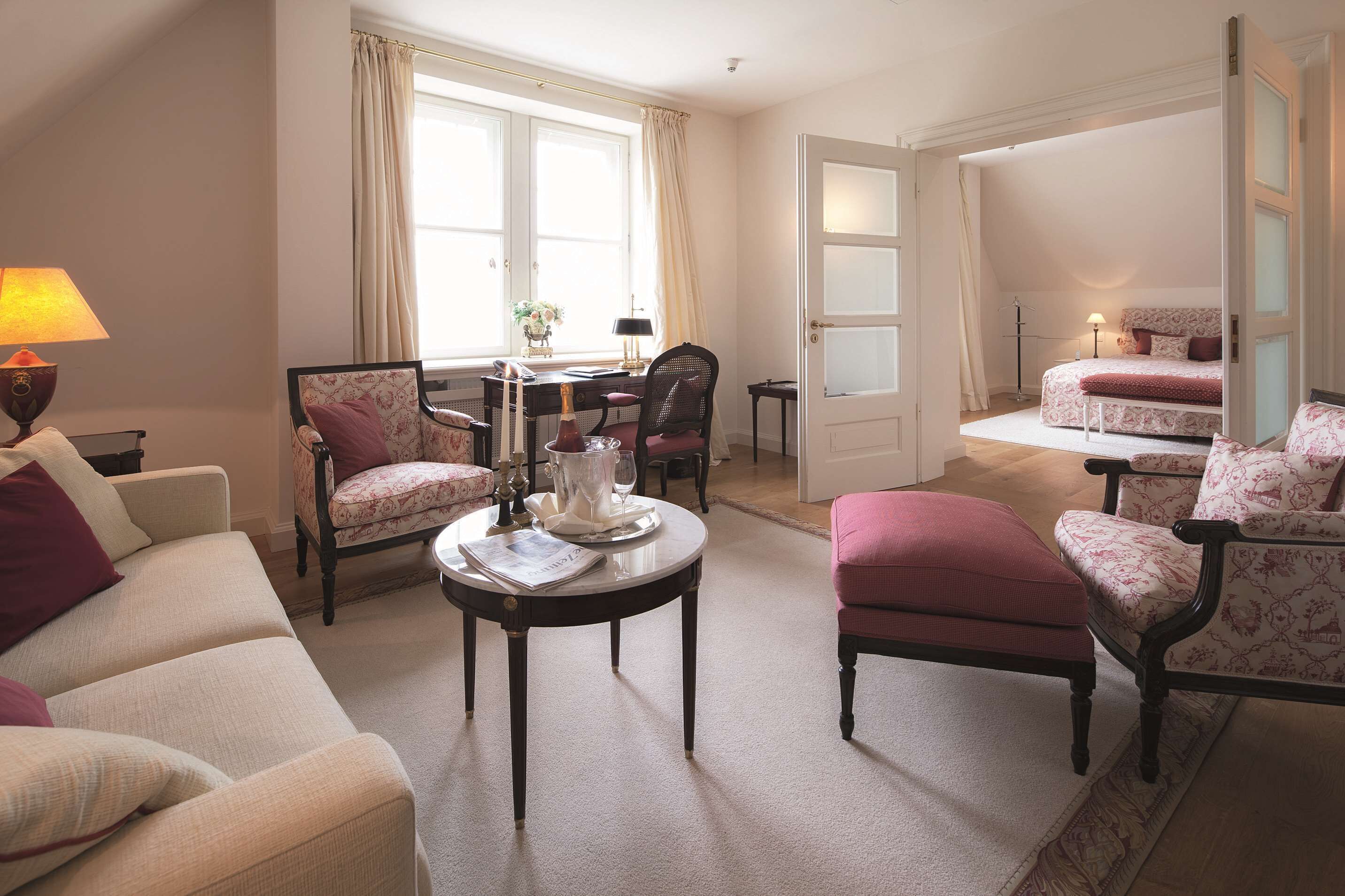 Una habitación luminosa y elegantemente amueblada, con un sofá, sillones, una mesita y una cama.