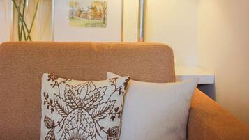A living room with a sofa, a lamp, a vase with flowers, and a framed picture on the wall.