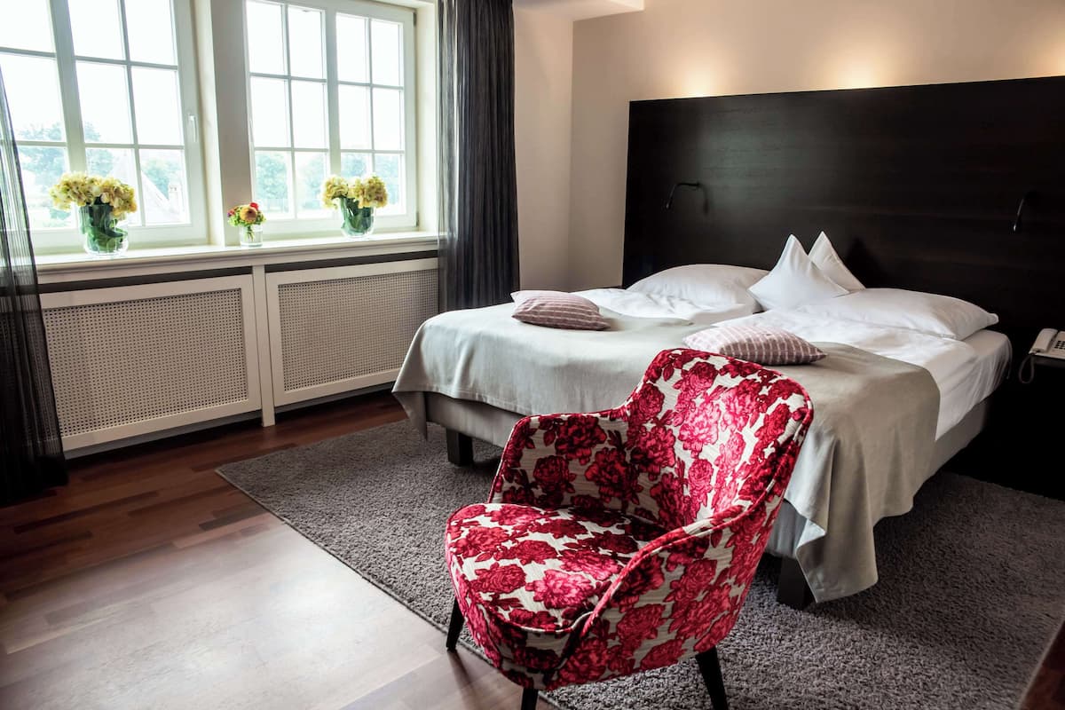 Een hotelkamer met een bed, een stoel, een raam met bloemen en een radiator.