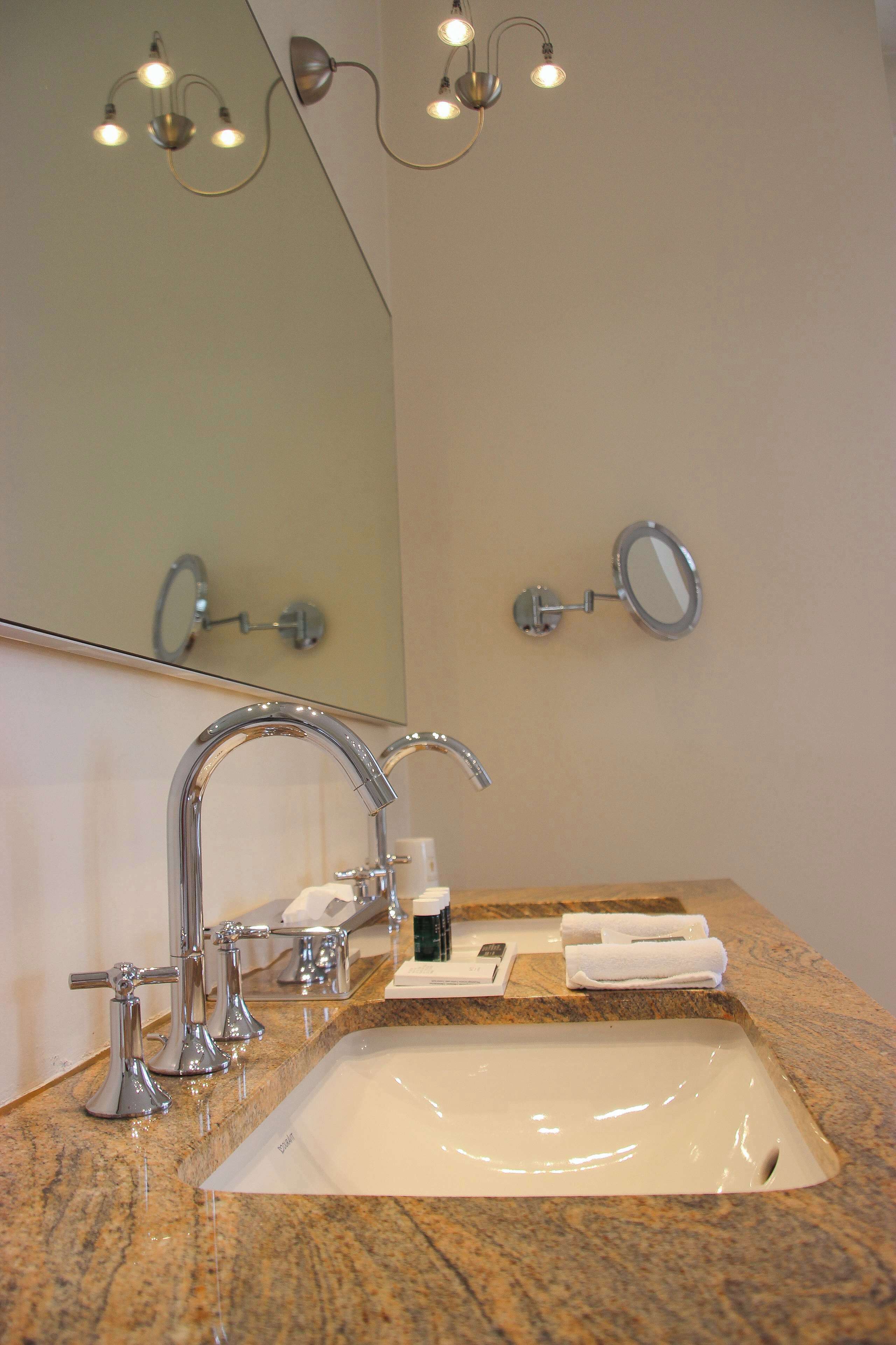 A bathroom with a granite countertop, a white sink, chrome fixtures, and a mirror with a round frame.