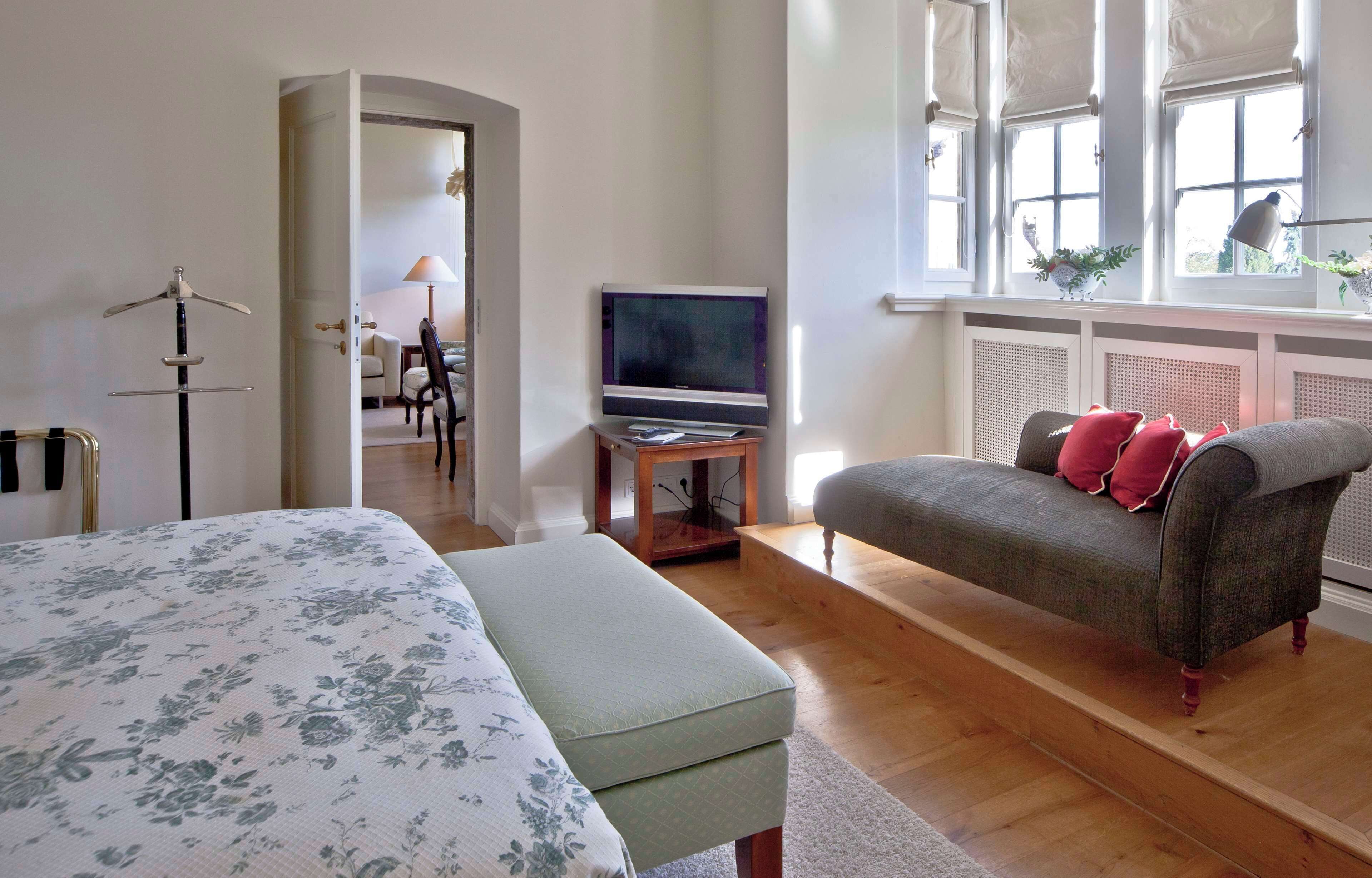 A bedroom with a bed, a chair, a TV, and a window with a view.