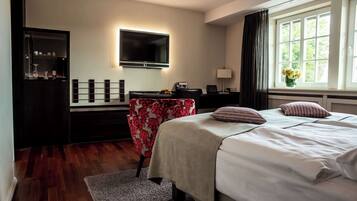 A hotel room with a bed, a desk with a computer, a TV mounted on the wall, and a window with curtains.