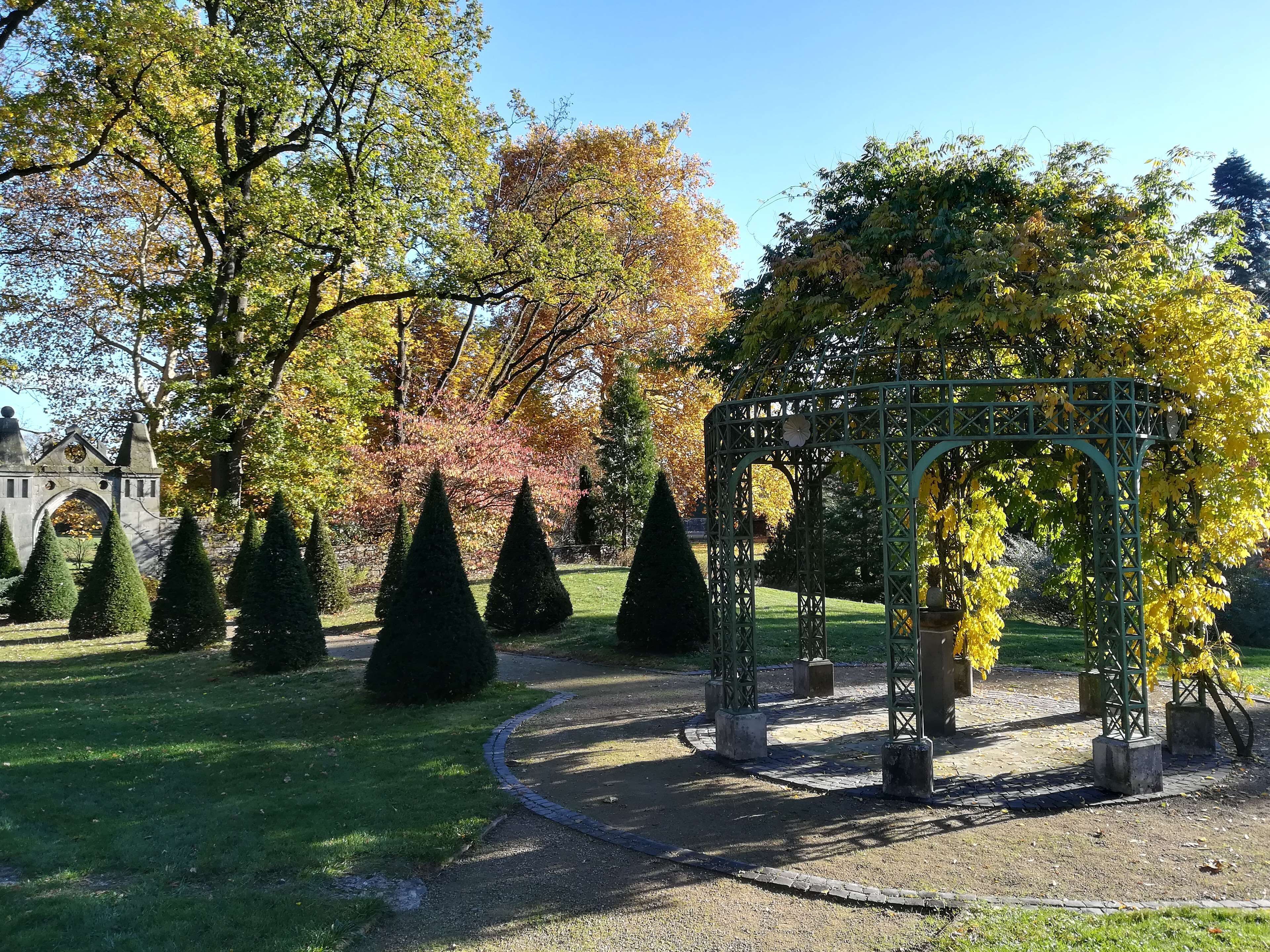 Un giardino con un gazebo, siepi curate e un arco in pietra.