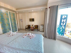 A hotel room with a large bed, two chairs, a small table, a TV, and a view of the outside.