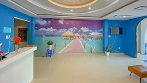 A hotel reception area with a mural of a tropical beach, a reception desk, and a staircase leading to the upper floor. - Phuoc Hai Hotel By The Moment (Ho Chi Minh City)