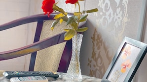 A marble table with a vase of red roses, a framed picture, and remote controls. - Phuoc Hai Hotel By The Moment (Ho Chi Minh City)