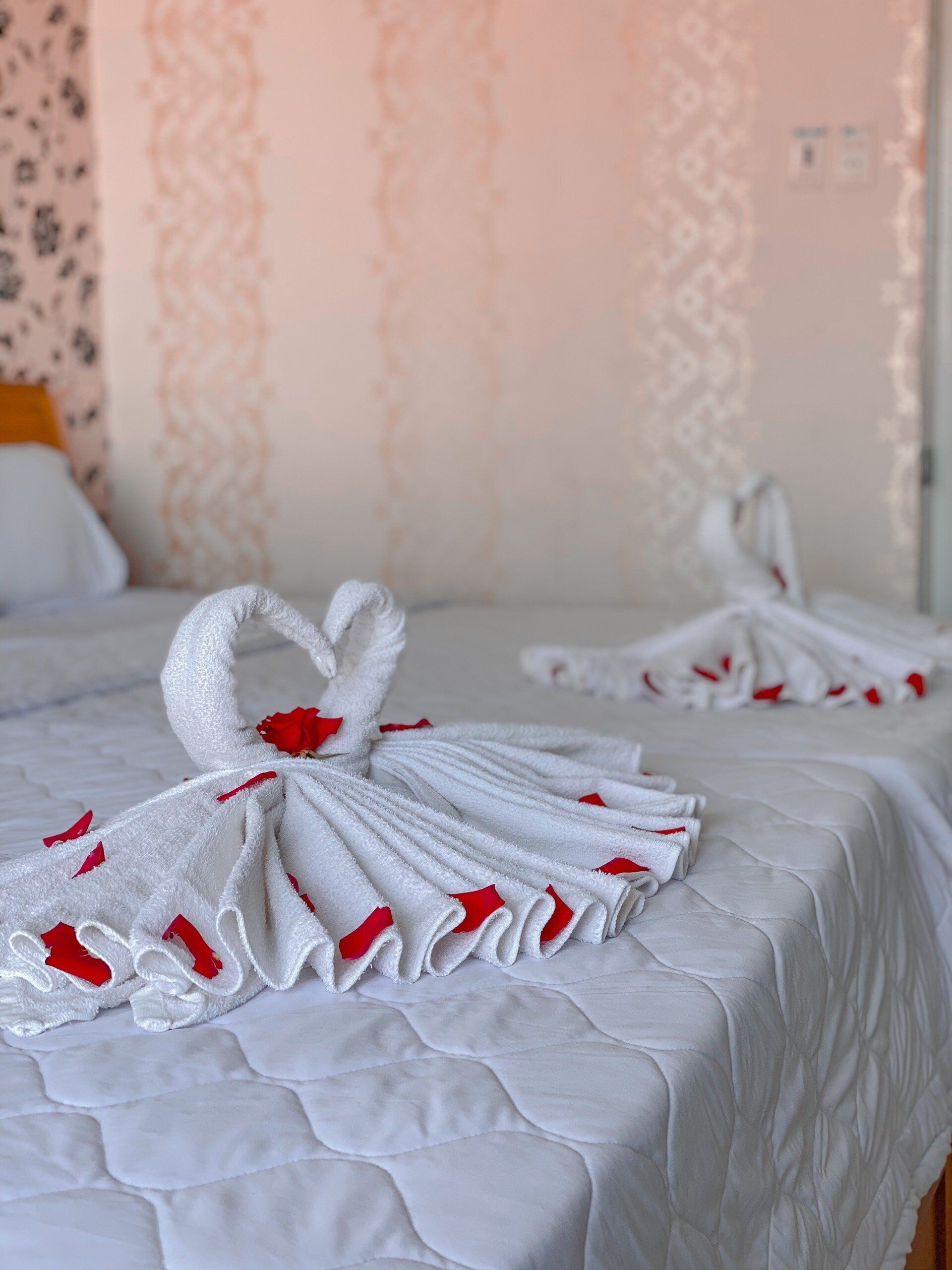 A hotel room with a neatly made bed featuring two towels arranged in a swan shape with red accents.