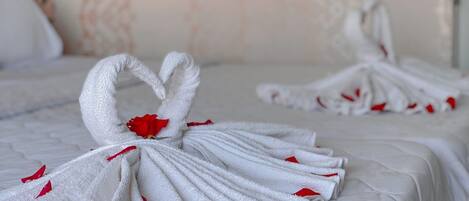 A hotel room with a neatly made bed featuring two towels arranged in a swan shape with red accents.