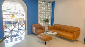 A modern interior with a blue accent wall, a brown leather sofa, a matching armchair, and a small table with a remote control. - Phuoc Hai Hotel By The Moment (Ho Chi Minh City)