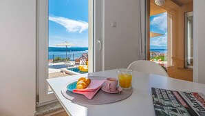 Een ontbijttafel met croissant, koffie en sinaasappelsap, met uitzicht op een zwembad en strand.