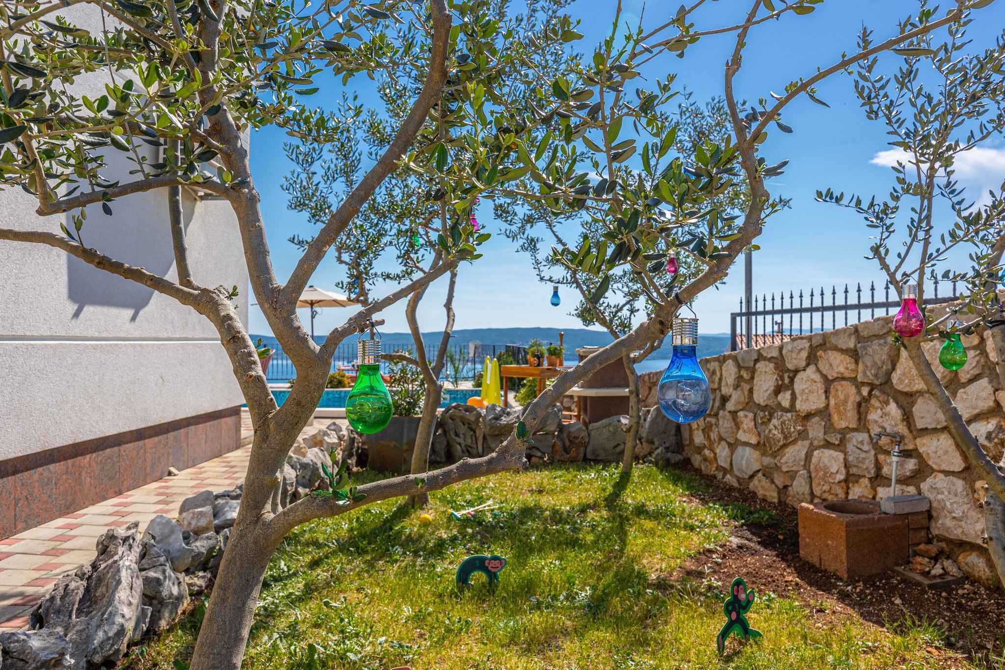 Ein Außenbereich mit einer Steinmauer, einem Baum und Blick aufs Meer.