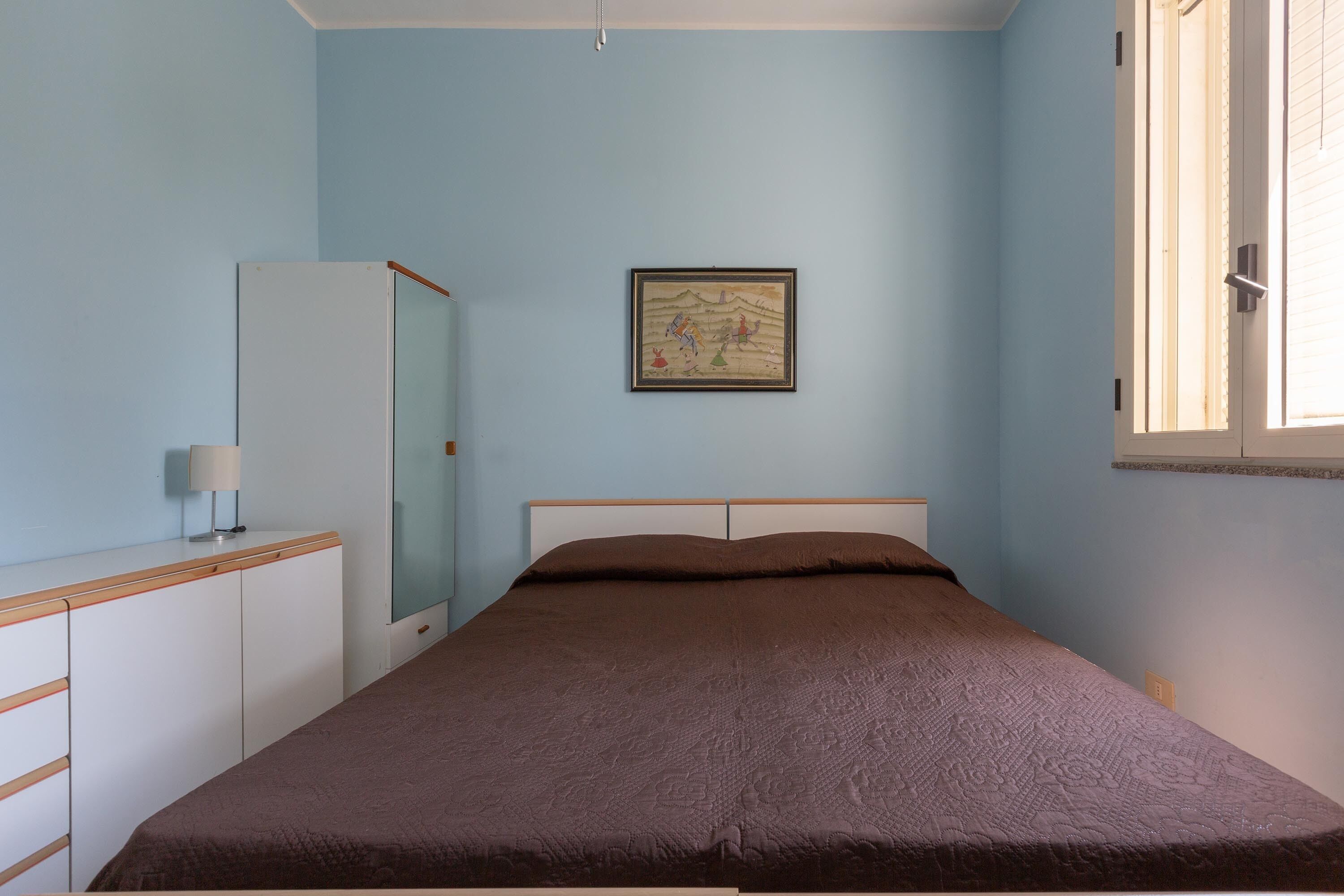 Un dormitorio con cama, armario, espejo y ventana.