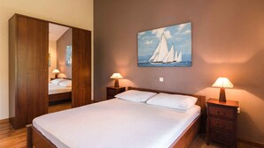A bedroom with a bed, wooden wardrobe, nightstands, and a painting of sailboats. - Holiday apartment with balcony and sea view (Selce)