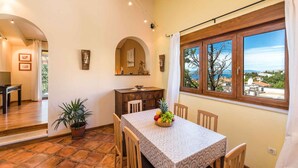 A dining area with a table set for four, a potted plant, and a view of the sea through a window. - Holiday apartment with balcony and sea view (Selce)