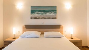Una camera da letto con un letto, due comodini, una lampada da comodino, un quadro appeso al muro raffigurante l'oceano e due luci a parete.