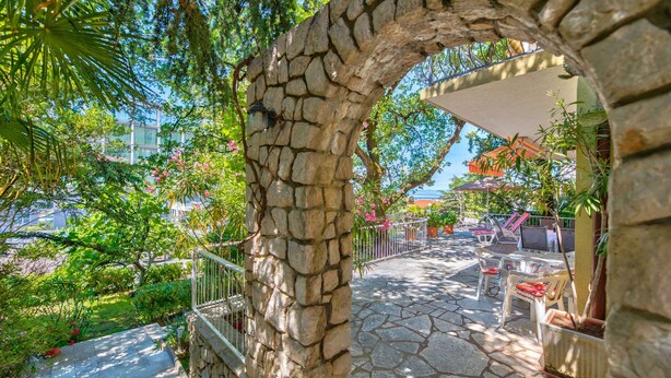 Un arco in pietra che dà accesso a un patio con posti a sedere all'aperto e vista su un edificio residenziale.