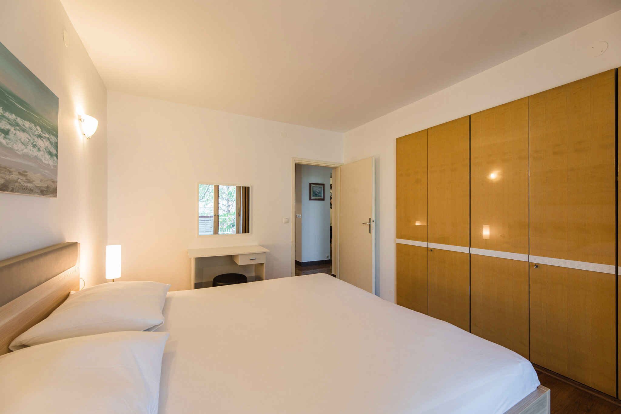 A bedroom with a bed, a bedside table, a wardrobe, and a painting on the wall.