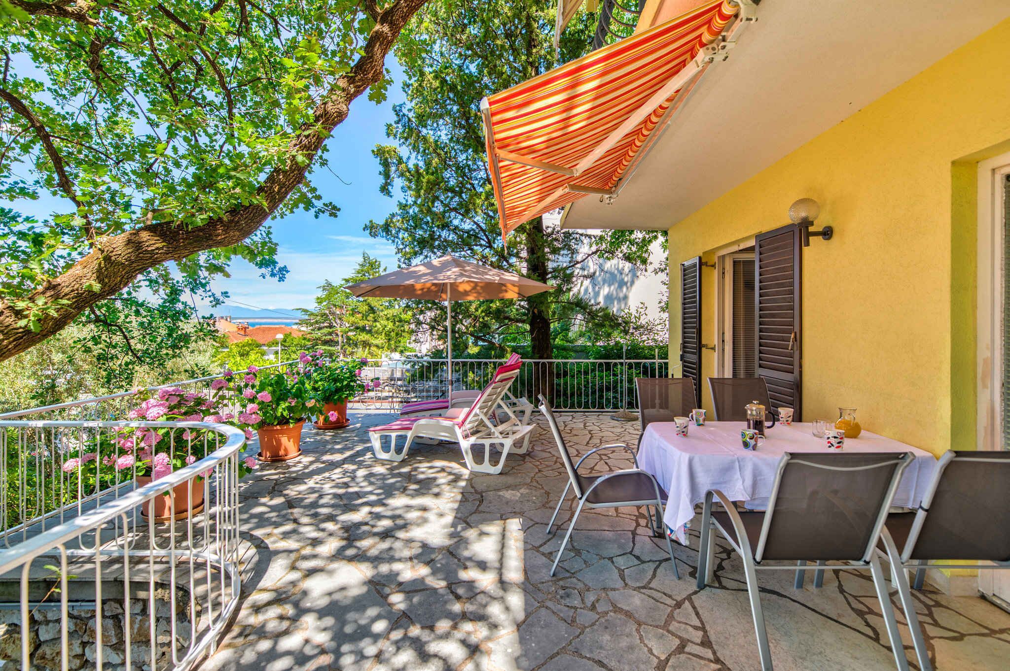 Une terrasse extérieure avec un sol en pierre, des rampes en métal blanc et des plantes en pot.