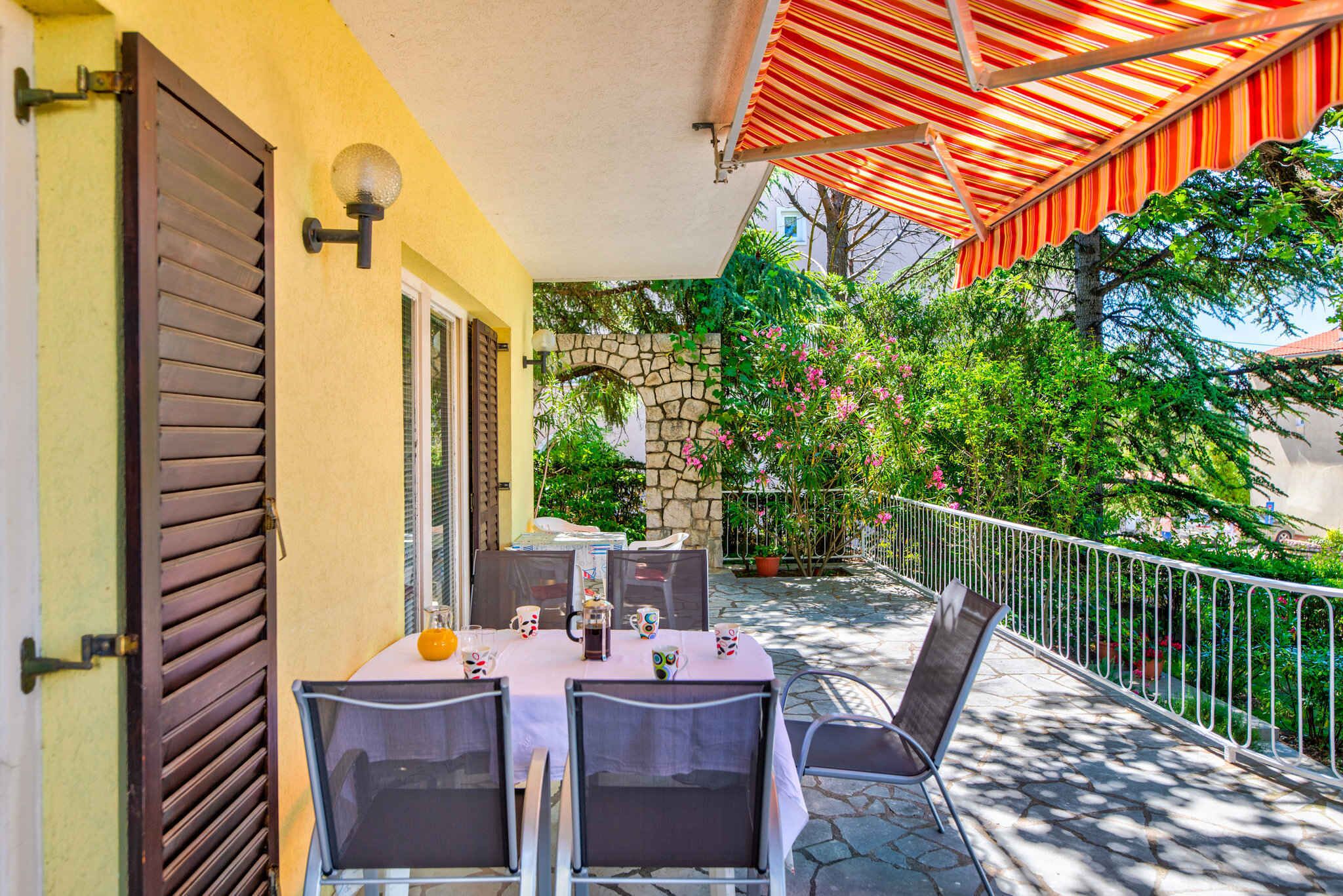 An outdoor patio with a table set for four, surrounded by chairs, a stone wall, and a railing.