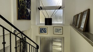 Uma escadaria com corrimão de metal, um quadro na parede, uma janela com ramos e fotografias emolduradas na parede.