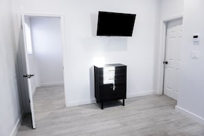 En hall med en svart byrå, en väggmonterad tv och vita dörrar.