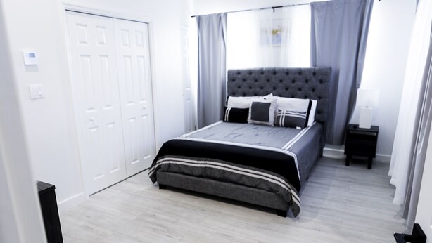 Een slaapkamer met een bed, nachtkastje, kledingkast en een raam met gordijnen.