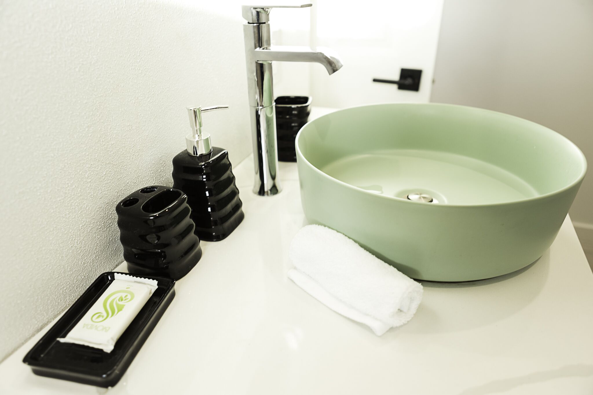 A bathroom with a white sink, a green basin, a black soap dispenser, a white towel, and a black soap container.
