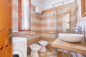A bathroom with a washing machine, two toilets, a sink, and a shower.