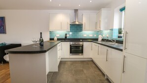 A modern kitchen with white cabinets, a black countertop, and a blue-tiled backsplash. - Hen Gapel (Caernarfon)