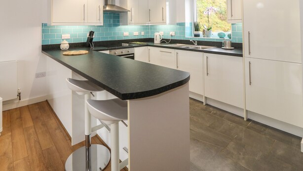 A modern kitchen with white cabinets, a black countertop, and a window with a view of greenery. - Hen Gapel (Caernarfon)