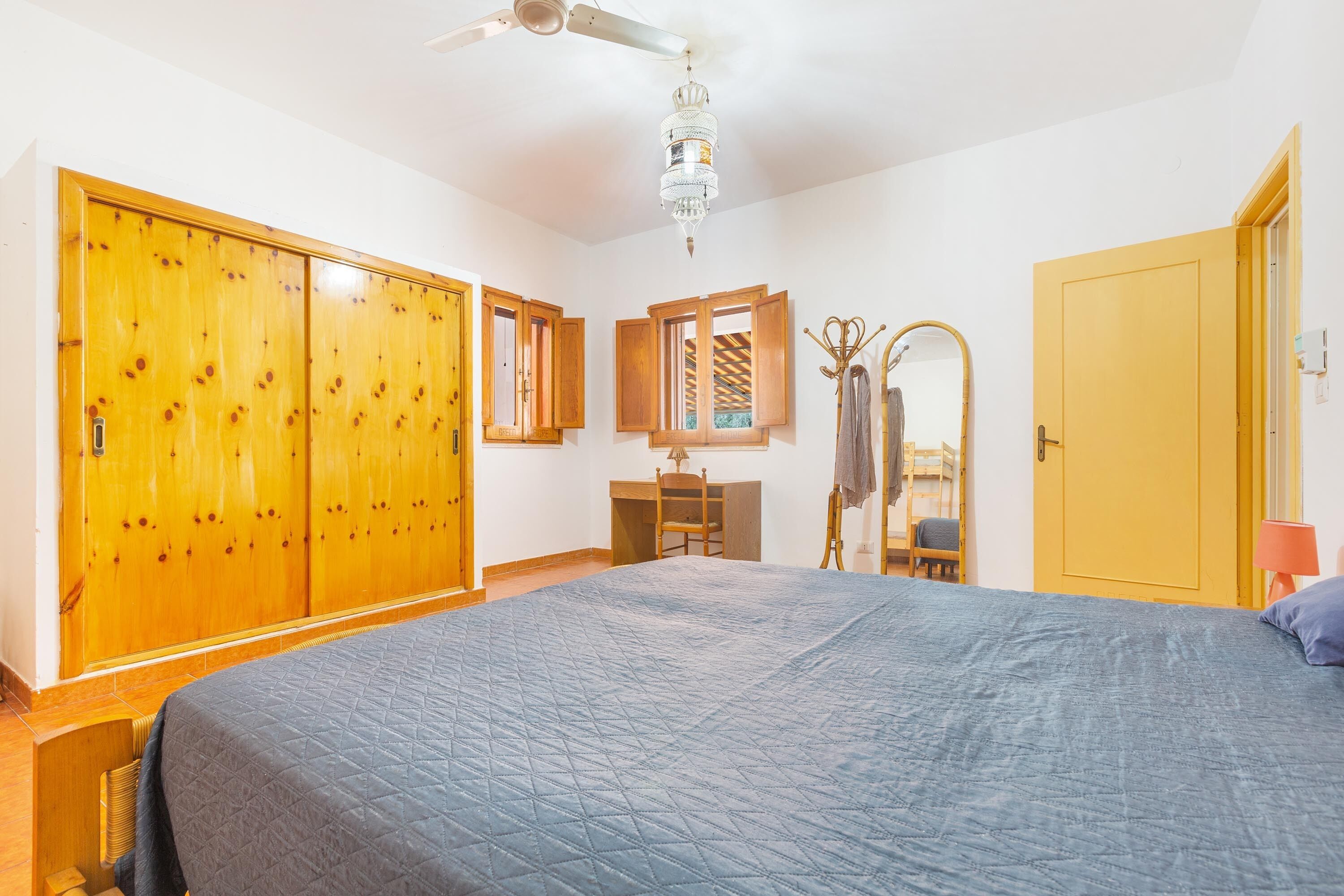 Une chambre avec un grand lit, une armoire en bois, un bureau et un ventilateur de plafond.