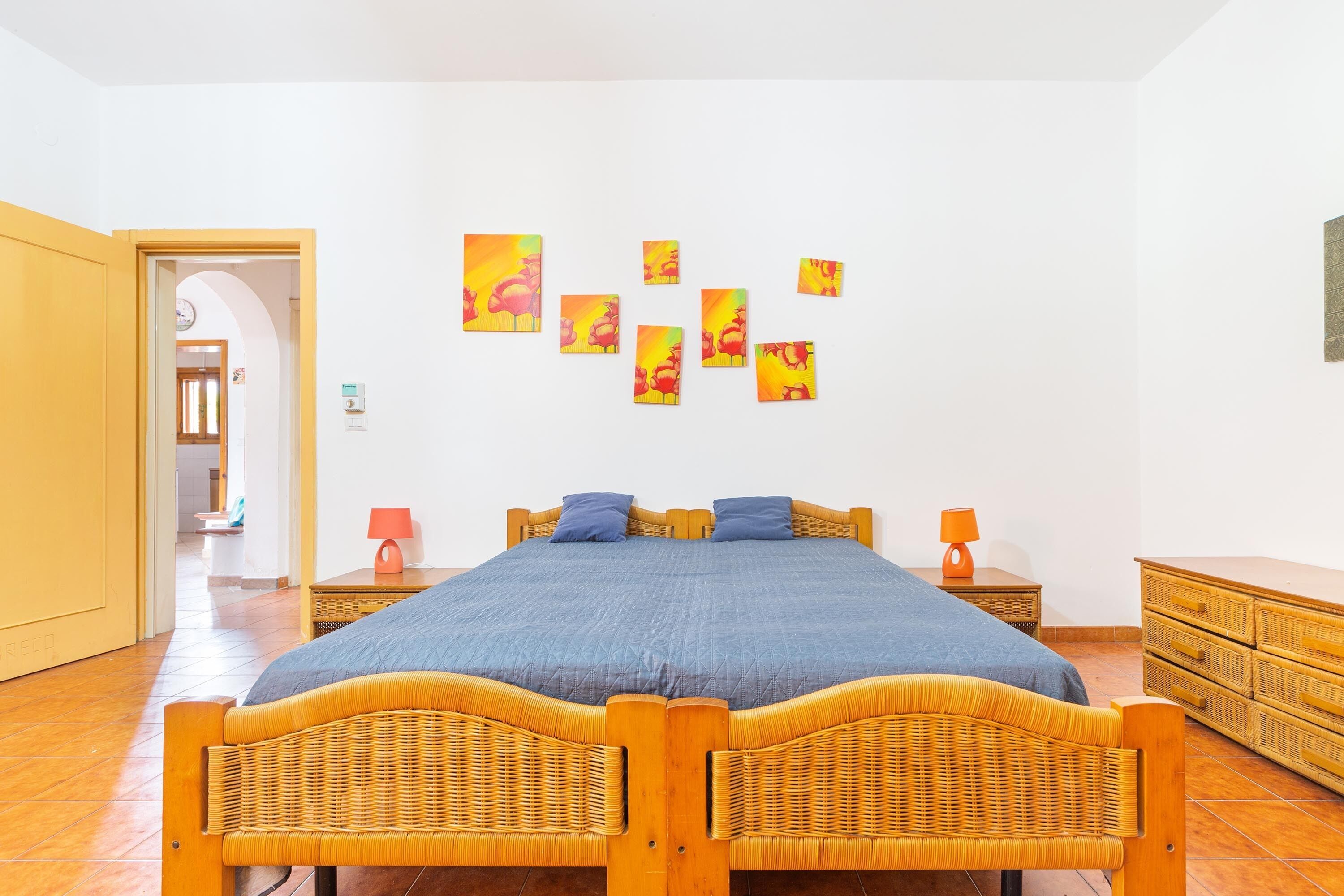 Un dormitorio con una cama doble, dos mesitas de noche, un aparador y una pared decorada con cuadros.