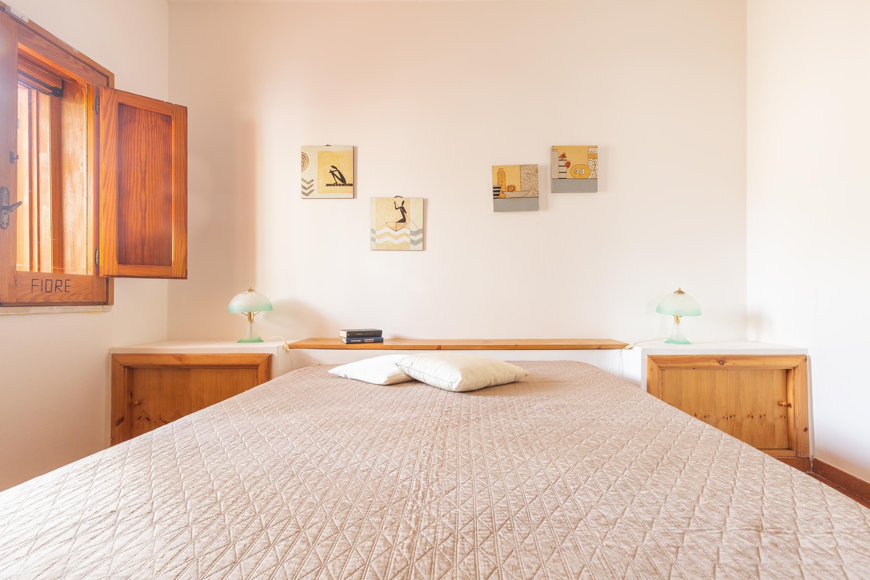 A bedroom with a large bed, two bedside tables, a wooden wardrobe, and three wall-mounted artworks.