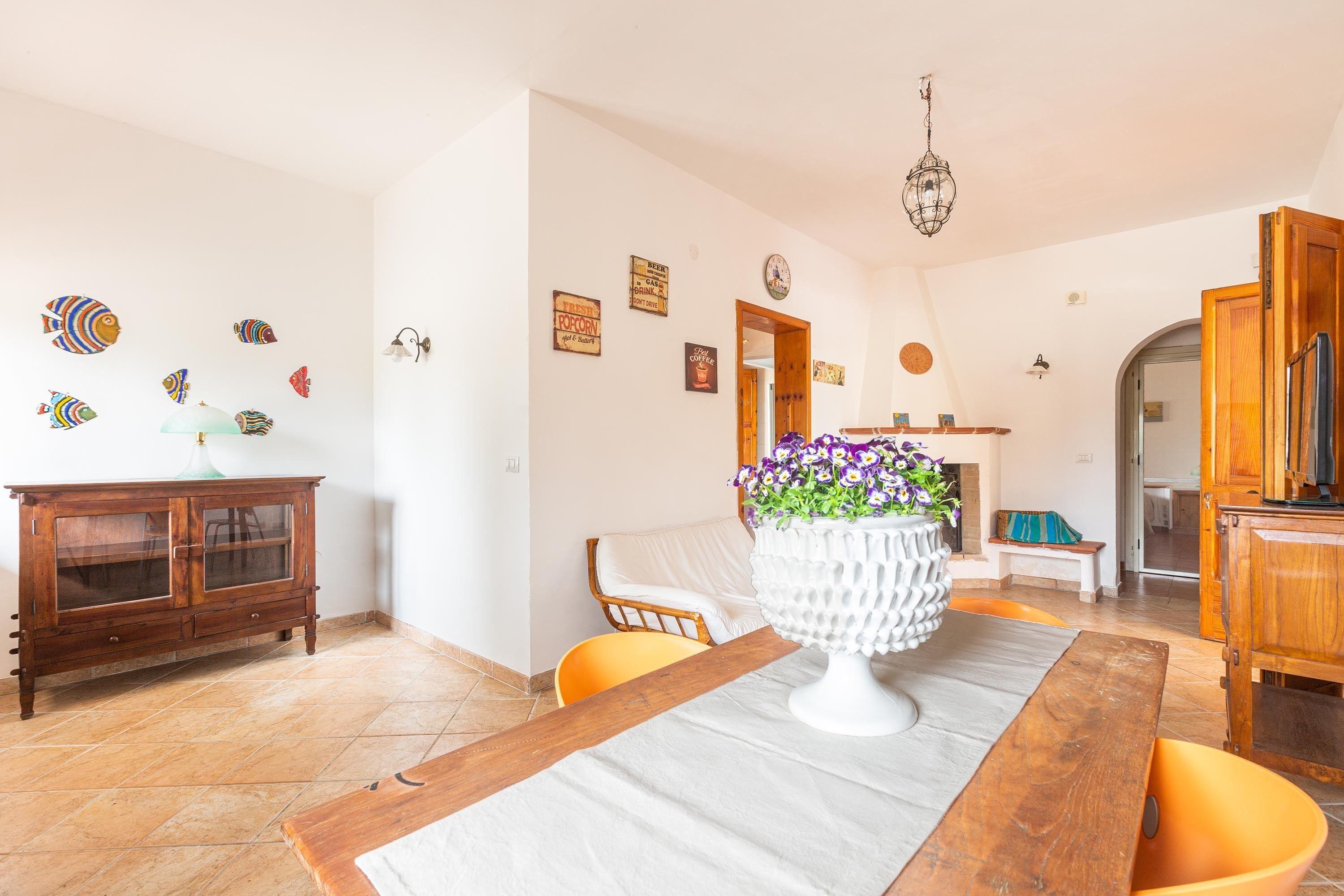 A dining area with a wooden table, chairs, a white vase with flowers, and a cabinet with glass doors.